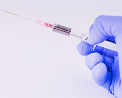 A hand with a blue glove holds a syringe and needle containing blood