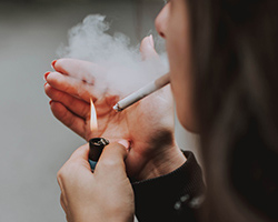 A woman holds a lighther up to a cigarette in her mouth