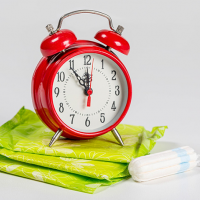 A red alarm clock sitting on top of a pile of green sanitary pads next to a tampon